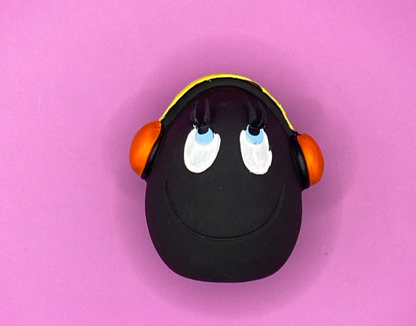 Huevo DJ de Látex de LANCO para perros de color negro con auriculares donde la parte de la diadema es amarilla y los altavoces son naranjas. Sus ojos son azules con la pupila en negro y están mirando hacia arriba como con cara de bueno, también  tiene una línea en la boca sonriendo 2