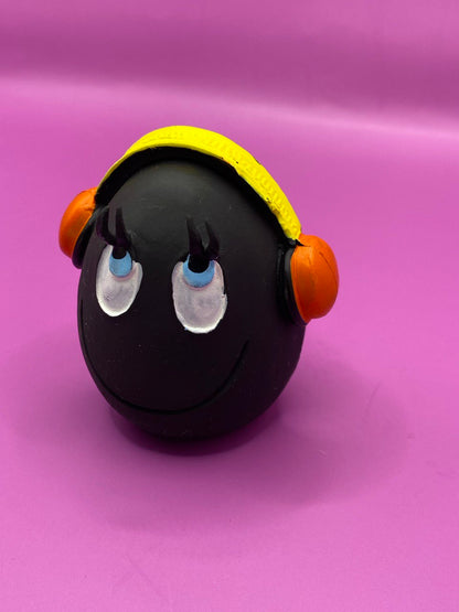 Huevo DJ de Látex de LANCO para perros de color negro con auriculares donde la parte de la diadema es amarilla y los altavoces son naranjas. Sus ojos son azules con la pupila en negro y están mirando hacia arriba como con cara de bueno, también  tiene una línea en la boca sonriendo 3