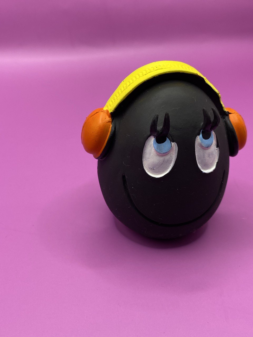 Huevo DJ de Látex de LANCO para perros de color negro con auriculares donde la parte de la diadema es amarilla y los altavoces son naranjas. Sus ojos son azules con la pupila en negro y están mirando hacia arriba como con cara de bueno, también  tiene una línea en la boca sonriendo 1